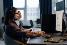 Dois programadores trabalham juntos em computadores em um escritório de tecnologia.