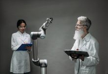 Dois pesquisadores trabalham juntos diante de um braço robótico em um laboratório de tecnologia.