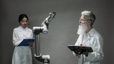 Dois pesquisadores trabalham juntos diante de um braço robótico em um laboratório de tecnologia.