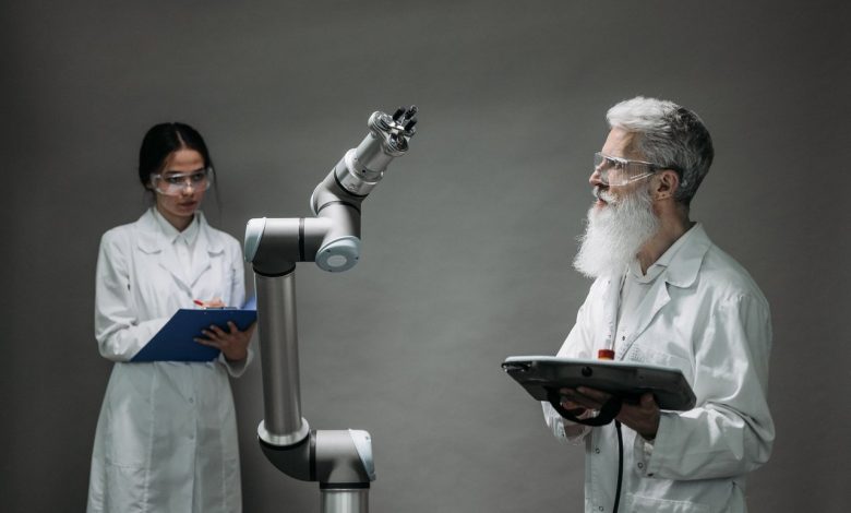 Dois pesquisadores trabalham juntos diante de um braço robótico em um laboratório de tecnologia.