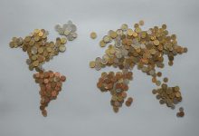 Mapa-múndi formado por moedas sobre fundo cinza, simbolizando transações e finanças globais